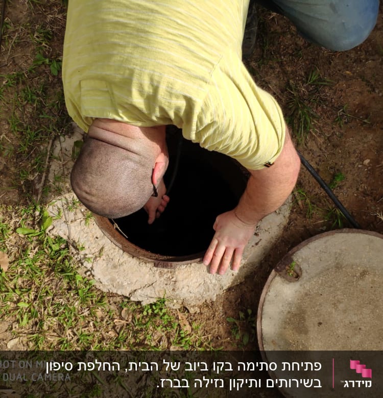 אדם בודק פתח ביוב עם מכסה פתוח
